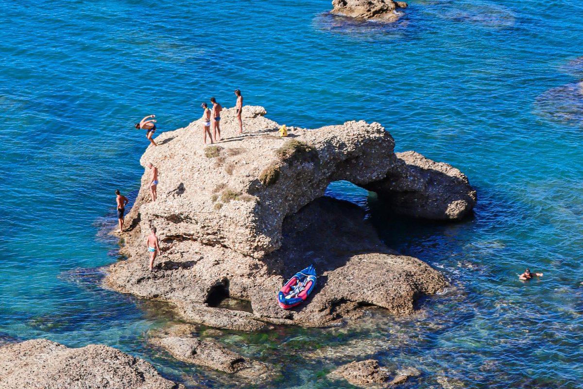 Swimmers on a rock arch, a kayak pulled up on the rock below